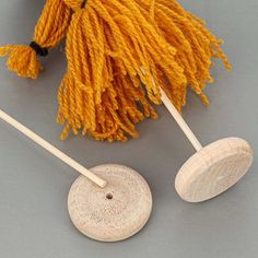 two wooden spoons with yarn on them sitting next to each other, one has a yellow tassel