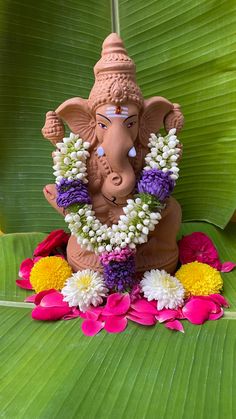 an elephant statue with flowers around it's neck sitting on a leafy surface