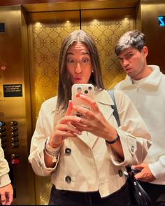 a woman taking a selfie with her cell phone in front of an elevator door