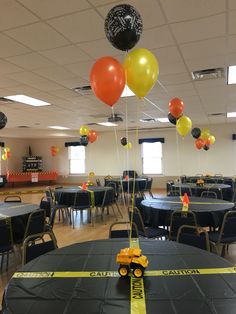 a room filled with tables and chairs covered in black tablecloths, yellow ribbon and balloons