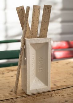 a white vase with rulers sticking out of it's sides on top of a wooden table