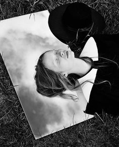 a black and white photo of a woman with long hair wearing a hat in the grass