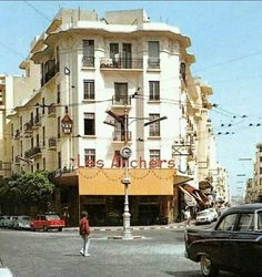 a man walking across a street in front of a tall building with balconies