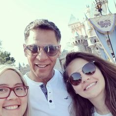 two women and a man posing for a photo in front of the castle at disneyland