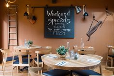 an empty restaurant with wooden tables and blue chairs in front of a chalkboard that says weekend specials