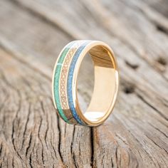 a gold ring with green and white wood inlays sits on a wooden surface