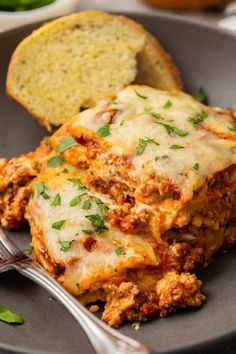 a plate topped with lasagna covered in sauce and cheese next to a slice of bread