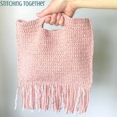 a hand holding a pink crocheted bag with fringes on it's sides