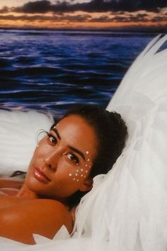 a woman laying on top of a bed covered in white sheets next to the ocean