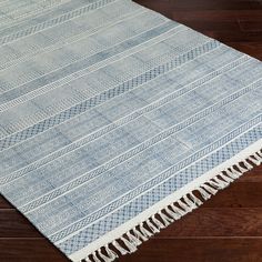 a blue and white area rug with fringes on the bottom, sitting on a wooden floor