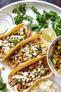 three tacos with corn, cilantro, and lime on a white plate