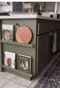 a wooden cutting board sitting on top of a kitchen counter next to a book shelf