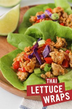 lettuce wraps filled with meat and vegetables on a wooden plate next to lime wedges