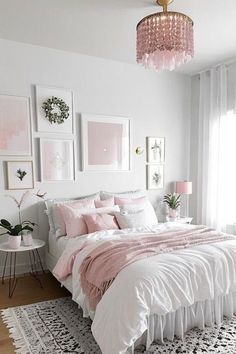 a white and pink bedroom with pictures on the wall above the bed, chandelier