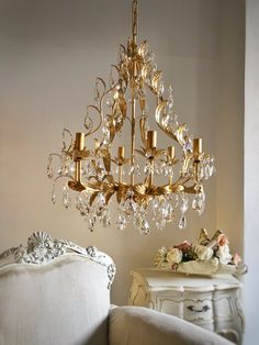 a chandelier hanging from the ceiling in a room with white furniture and flowers