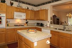 a large kitchen with wooden cabinets and granite counter tops, along with a bowl of fruit on the island