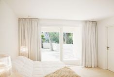 a white bed sitting in a bedroom next to a window with curtains on the outside