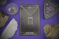 the sun tarot card necklace surrounded by crystals and other items on a purple background