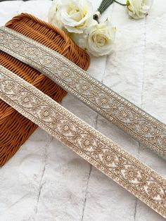 two silver and gold colored belts sitting on top of a white blanket next to flowers