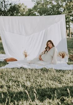 a woman sitting on the grass in front of an open white sheet with her legs crossed