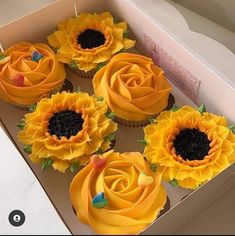 cupcakes with yellow frosting and sunflower decorations in a box on a table