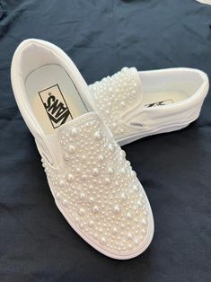 a pair of white slippers with pearls on them sitting on top of a bed