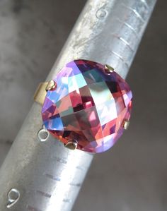 "Absolutely stunning shimmer and visual depth in this spectacular Swarovski crystal ring... Layers of delicious, juicy color and flashes of sparkle... Warm and romantic peachy, rose pink hues blossom in the background, while cool shimmering violet, blue and aqua flashes reflect off the surface of this uniquely faceted, rare Swarovski crystal. The vintage-style antiqued brass plated ring band comfortably fits sizes 6 to 10. - Cushion-cut Swarovski crystal: 16mm square (5/8\") - Comfortable antiqu Elegant Iridescent Rings For Parties, 2023 Wishlist, Vintage Kiss, Swarovski Crystal Rings, Crystal Ring, Large Crystals, Faceted Crystal, Ring Band, Crystal Rings