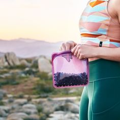 a woman holding a purple container filled with blueberries in her hands while standing next to some rocks