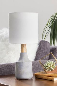 a table lamp sitting on top of a wooden table next to a white pillow and potted plant