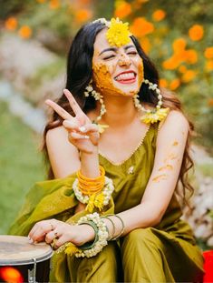 a woman sitting on the ground with her face painted like a sunflower and holding a drum