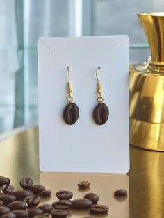 a pair of earrings sitting on top of a table next to coffee beans and a gold cup