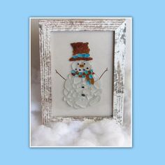 a snowman made out of glass sitting in a white frame on top of clouds