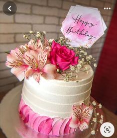 a white cake with pink flowers and a happy birthday sign on it's side