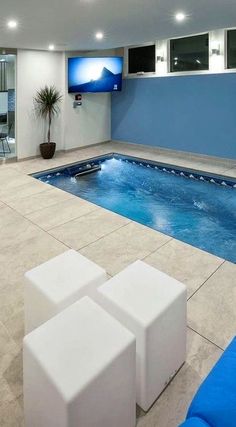 an indoor swimming pool with blue walls and white furniture in the foreground is a television