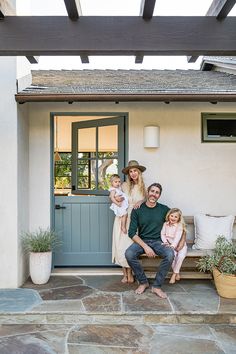 a man, woman and two children sitting on a bench in front of a house