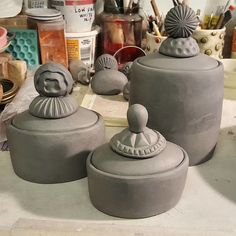 three gray ceramic containers sitting on top of a table next to other pottery and knick knacks