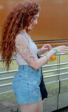 a woman with red hair and tattoos standing next to a train holding something in her hand