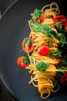 pasta with spinach, tomatoes and basil on a black plate ready to be eaten