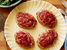 three meat patties on a white plate next to a bowl of salad and utensils