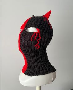 a knitted black and red mask on top of a white mannequin head