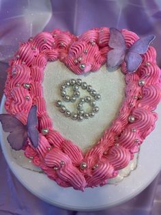 a heart shaped cake decorated with pink icing and purple butterflies on a white plate