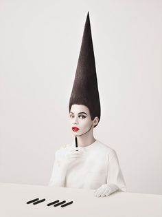 a woman sitting at a table with a pen in her hand and an odd hat on her head