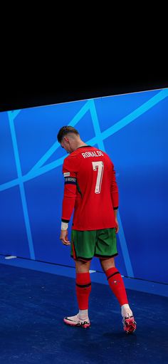 a man in red and green soccer uniform standing next to a blue wall