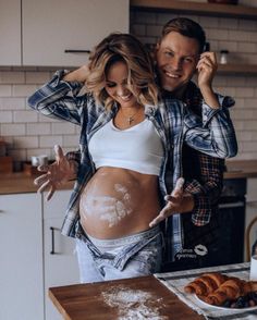 a pregnant woman standing next to a man in the kitchen