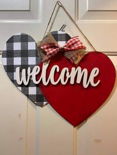 a heart shaped welcome sign hanging on the front door with a bow attached to it