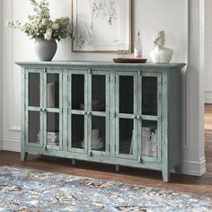 a blue cabinet with glass doors and vases on top of it next to a rug