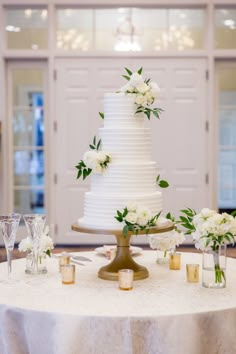 a white wedding cake sitting on top of a table next to wine glasses and flowers