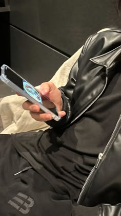 a person in a black leather jacket is holding a cell phone and looking at it