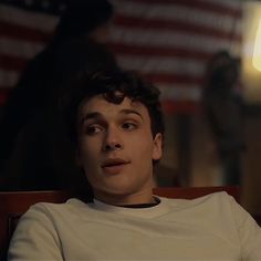 a young man sitting in front of an american flag