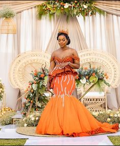 a woman in an orange dress standing next to a white chair with flowers on it